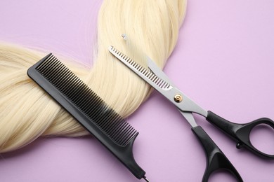 Photo of Blonde hair strand, comb and professional scissors on violet background, top view