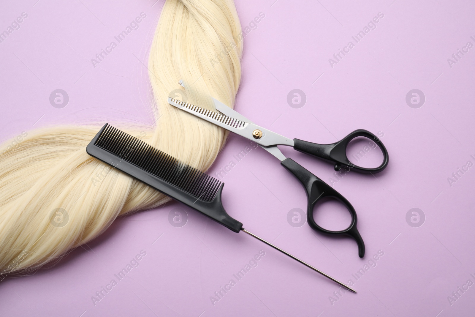 Photo of Blonde hair strand, comb and professional scissors on violet background, top view