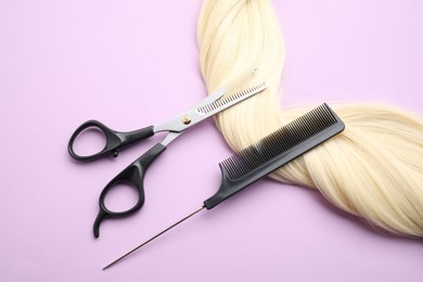 Photo of Blonde hair strand, comb and professional scissors on violet background, top view