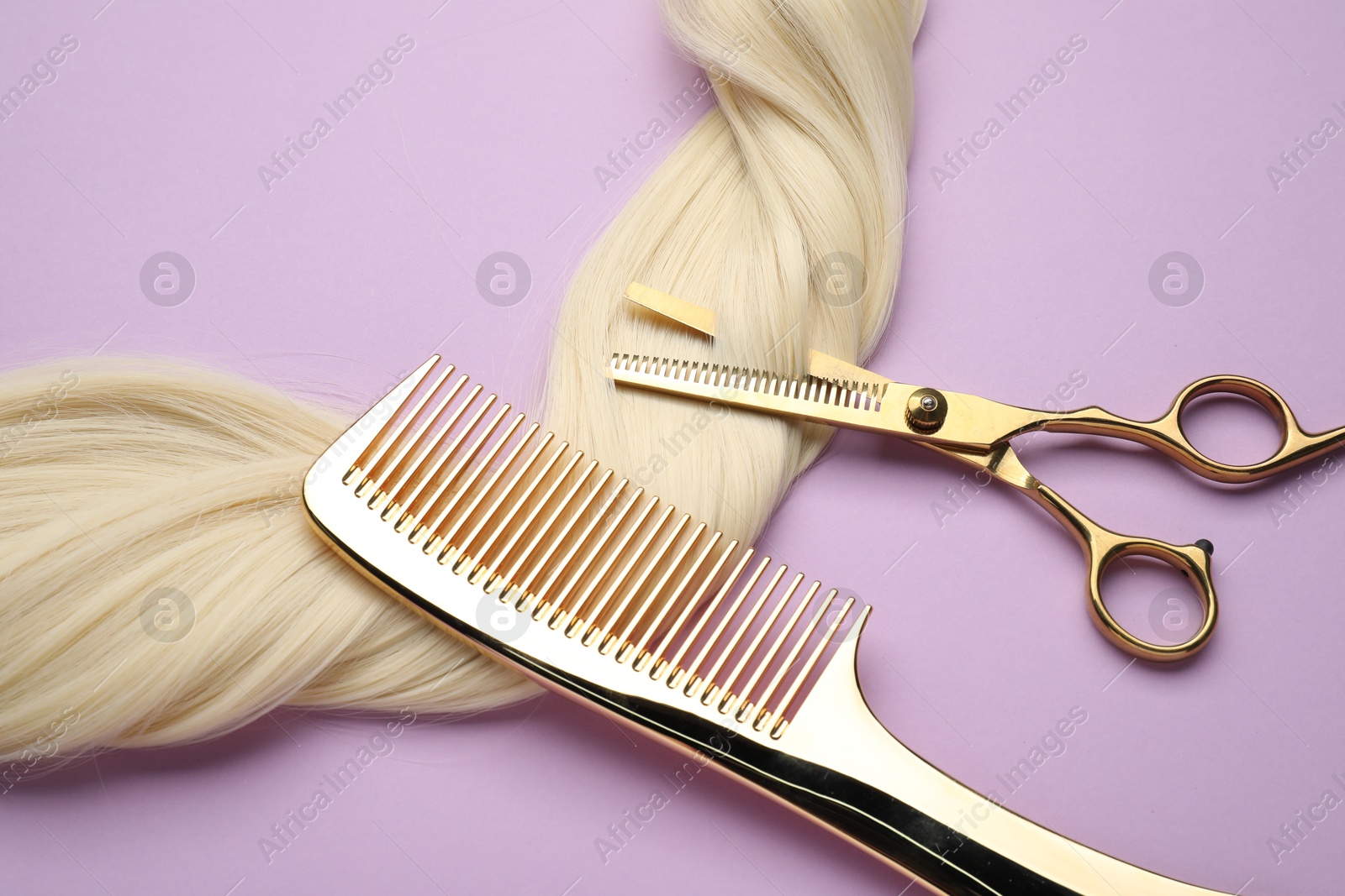 Photo of Blonde hair strand, comb and professional scissors on violet background, top view