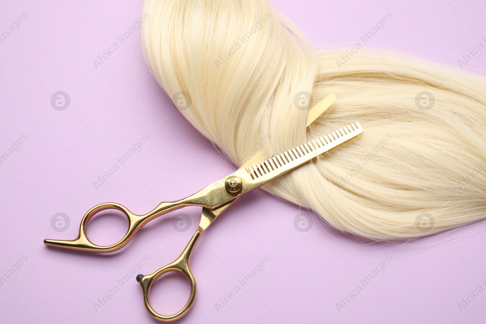 Photo of Blonde hair strand and professional scissors on violet background, top view