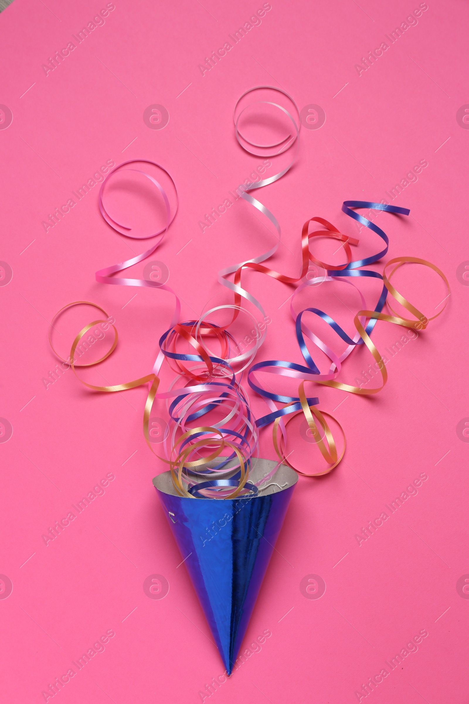 Photo of Blue party hat with streamers on bright pink background, top view