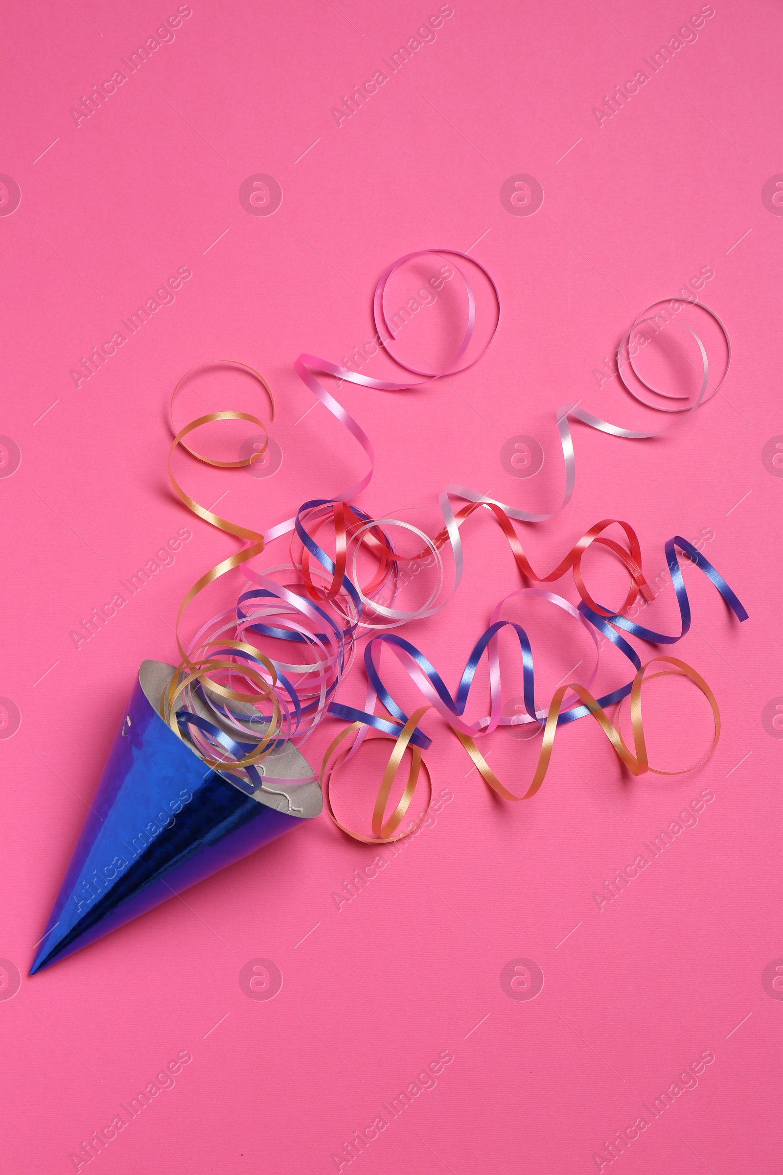 Photo of Blue party hat with streamers on bright pink background, top view