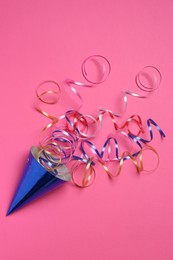 Blue party hat with streamers on bright pink background, top view