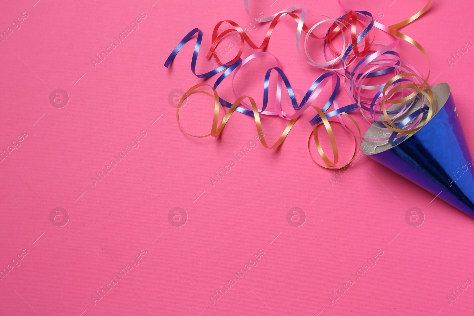 Photo of Blue party hat with streamers on bright pink background, top view. Space for text