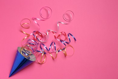 Blue party hat with streamers on bright pink background, top view. Space for text