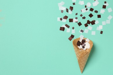 Shiny golden confetti flying out of ice cream cone on turquoise background, top view. Space for text