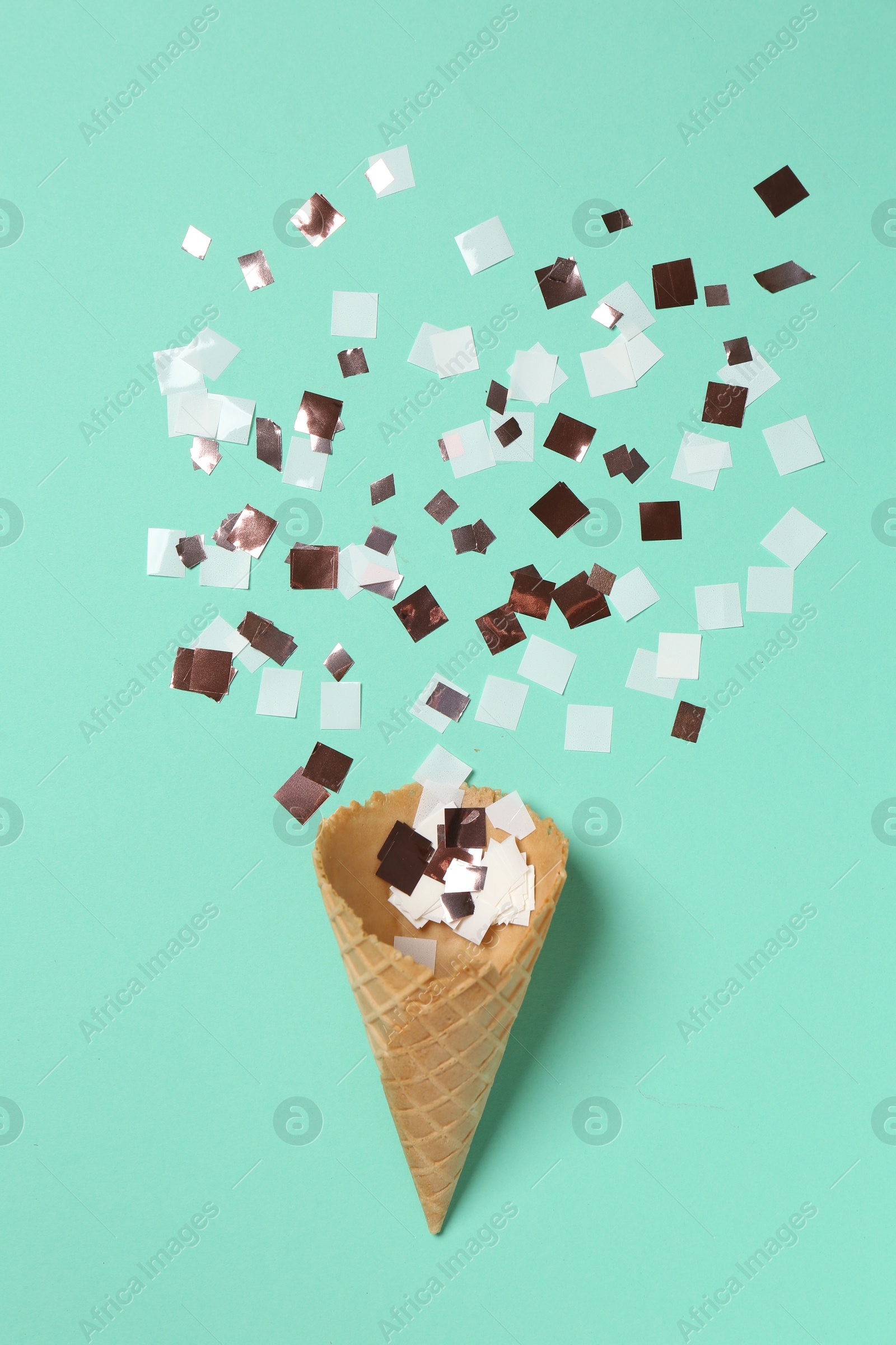 Photo of Shiny golden confetti flying out of ice cream cone on turquoise background, top view