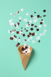 Shiny golden confetti flying out of ice cream cone on turquoise background, top view