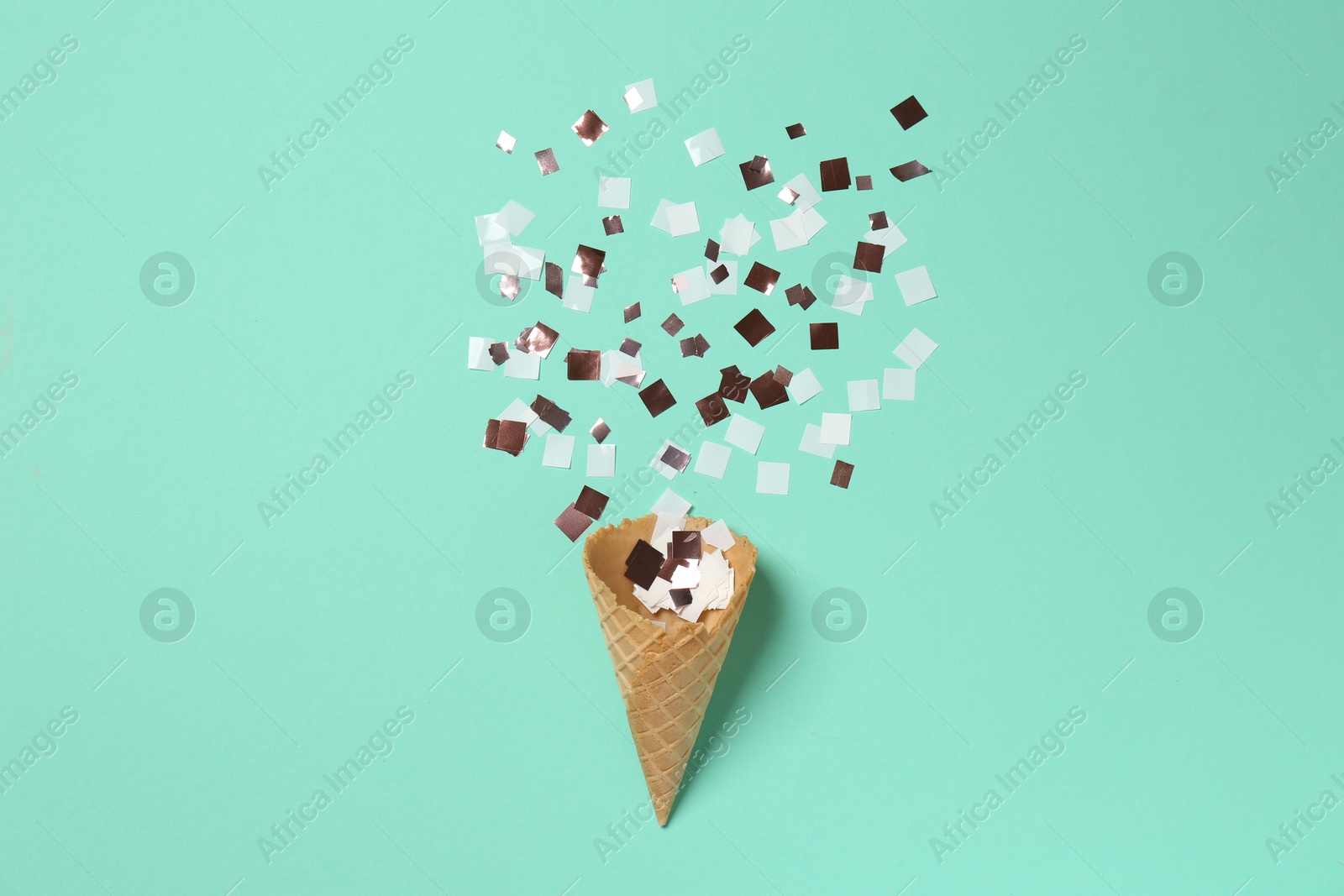 Photo of Shiny golden confetti flying out of ice cream cone on turquoise background, top view