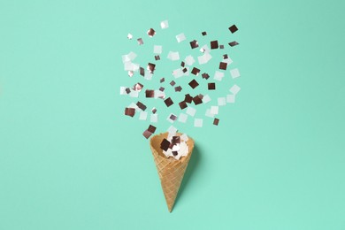 Photo of Shiny golden confetti flying out of ice cream cone on turquoise background, top view