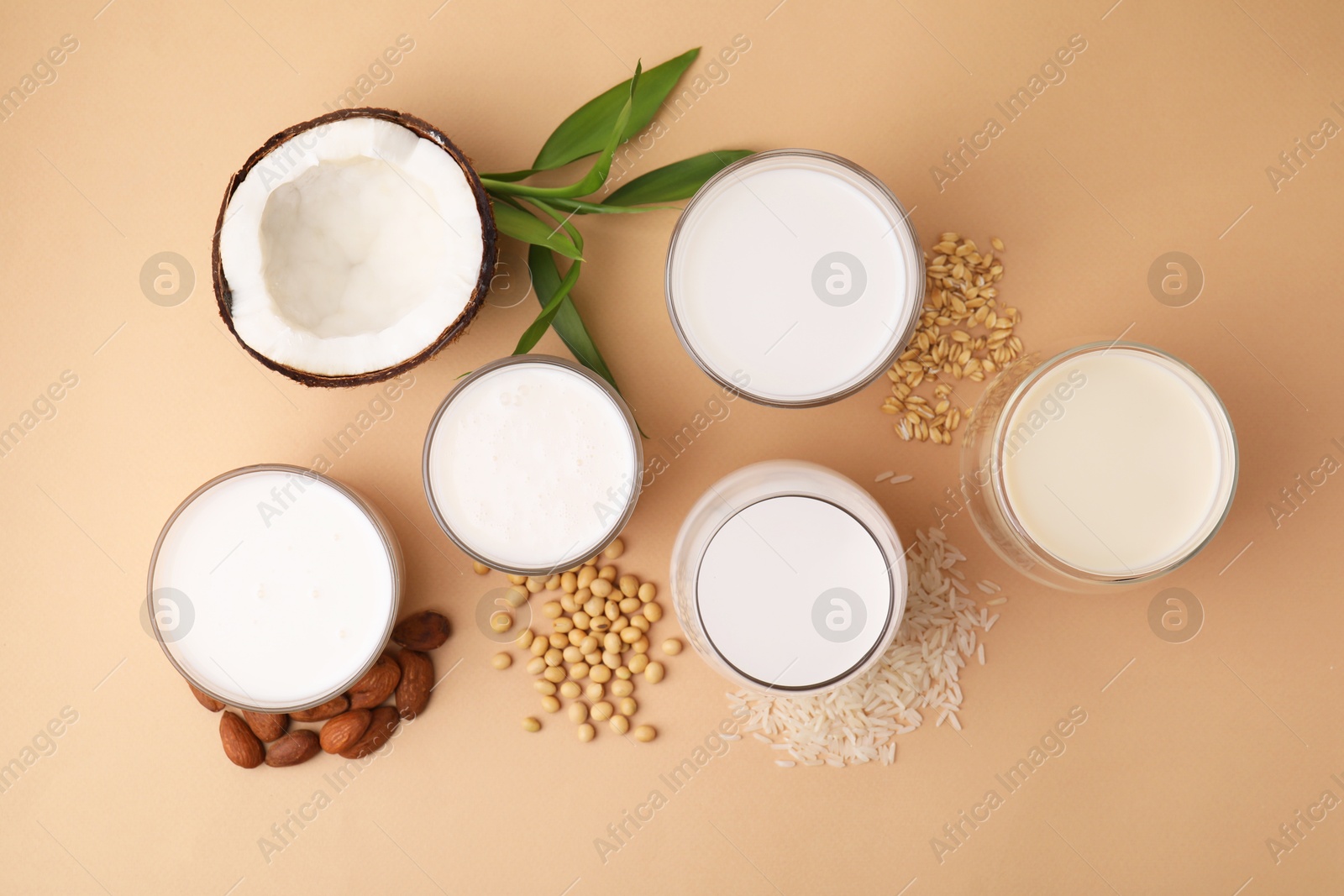 Photo of Different types of vegan milk and ingredients on beige table, flat lay