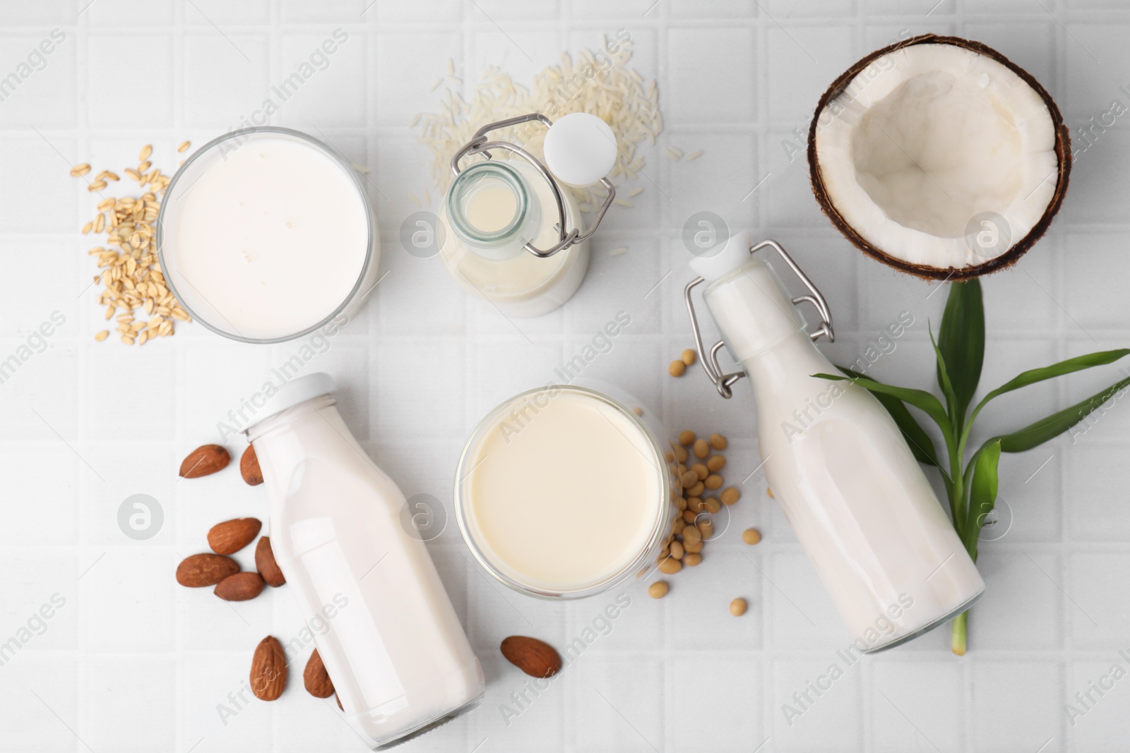 Photo of Different types of vegan milk and ingredients on white tiled table, flat lay