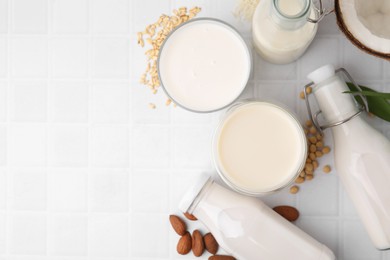 Different types of vegan milk and ingredients on white tiled table, flat lay. Space for text