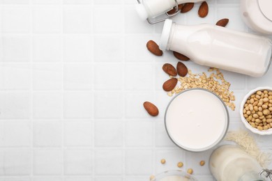 Photo of Different types of vegan milk and ingredients on white tiled table, flat lay. Space for text