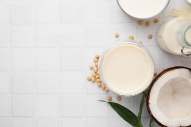 Photo of Different types of vegan milk and ingredients on white tiled table, flat lay. Space for text