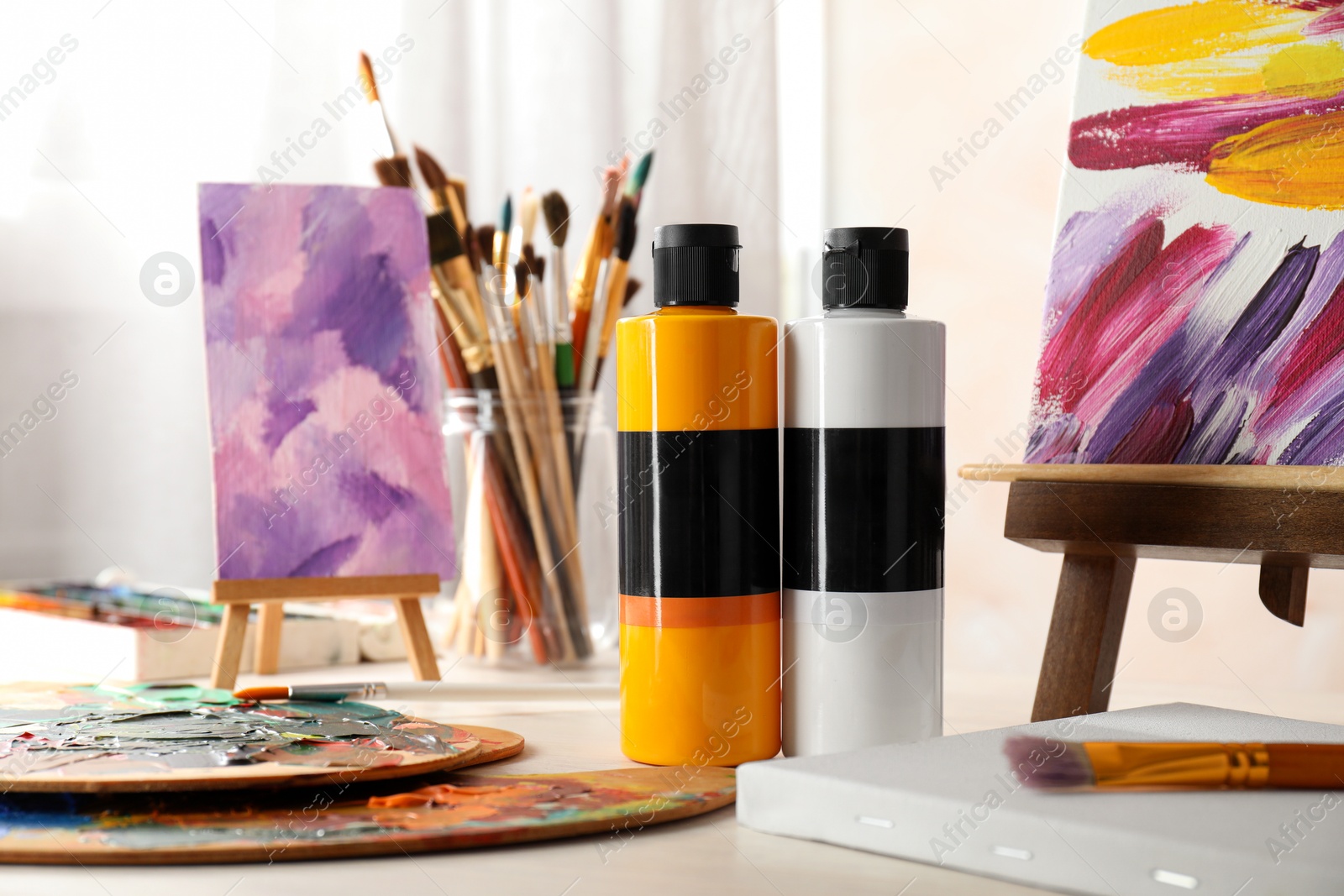 Photo of Acrylic paints of different colors, small easels, palettes and brushes on light table indoors