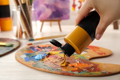 Woman mixing paints on palette at wooden table indoors, closeup