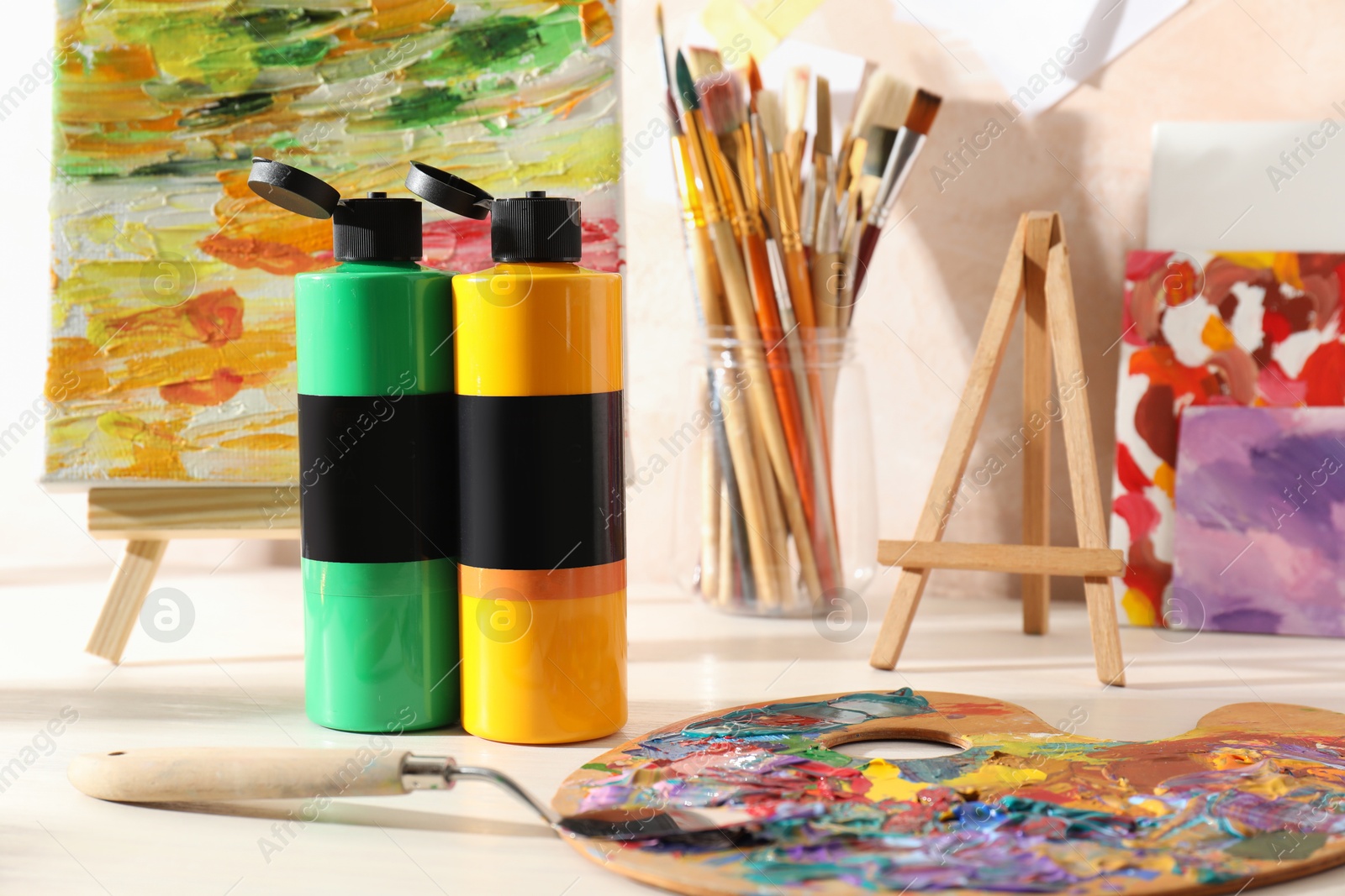 Photo of Acrylic paints of different colors, palette, knife, brushes and small easel with abstract picture on wooden table