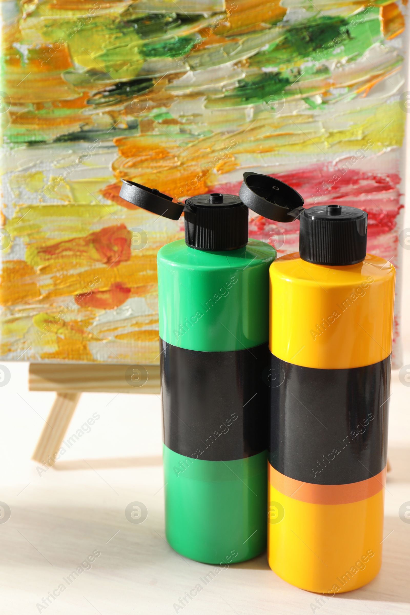 Photo of Acrylic paints of different colors and small easel with abstract picture on wooden table