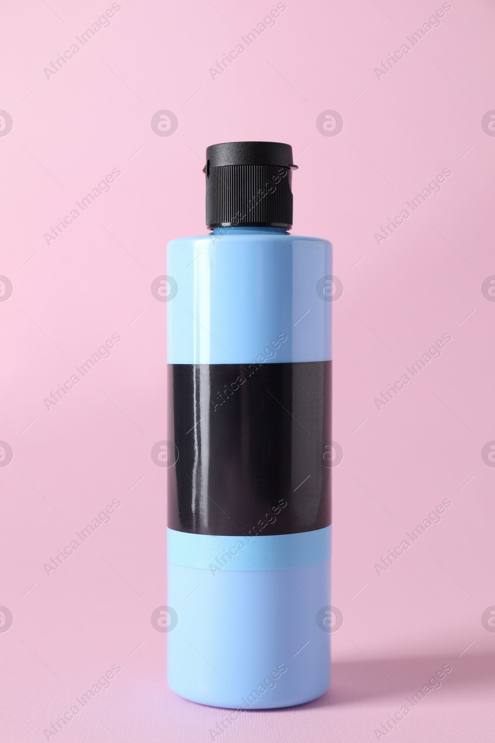 Photo of Light blue acrylic paint in bottle on pink background