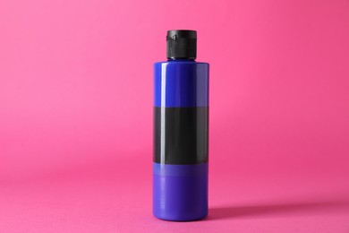 Photo of Blue acrylic paint in bottle on pink background