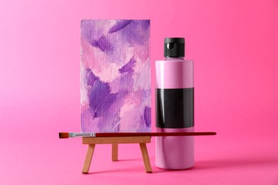 Photo of Acrylic paint in bottle, small easel with abstract picture and brush on pink background