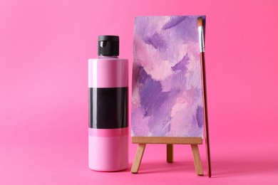 Photo of Acrylic paint in bottle, small easel with abstract picture and brush on pink background