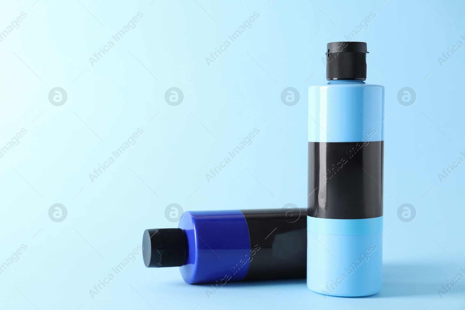 Photo of Acrylic paints of different colors on light blue background, space for text