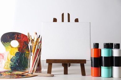 Photo of Acrylic paints of different colors, small easel, palettes and brushes on wooden table