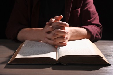 Photo of Man with Bible praying at wooden table, closeup