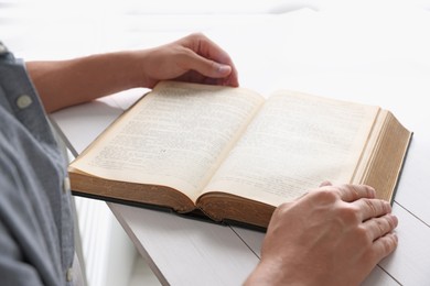 Photo of Man with Bible at white wooden table, closeup