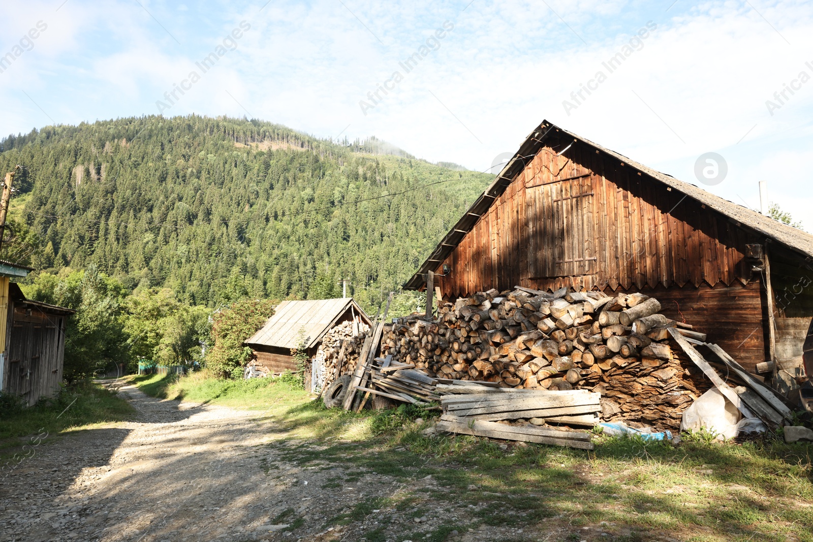 Photo of Stacked cut firewood near wooden house on sunny day