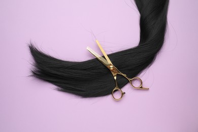 Photo of Black hair strand and professional scissors on violet background, top view