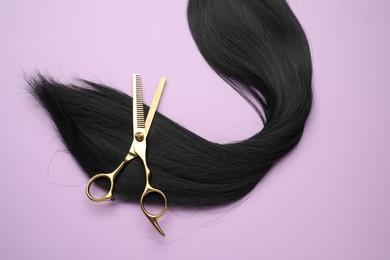 Photo of Black hair strand and professional scissors on violet background, top view