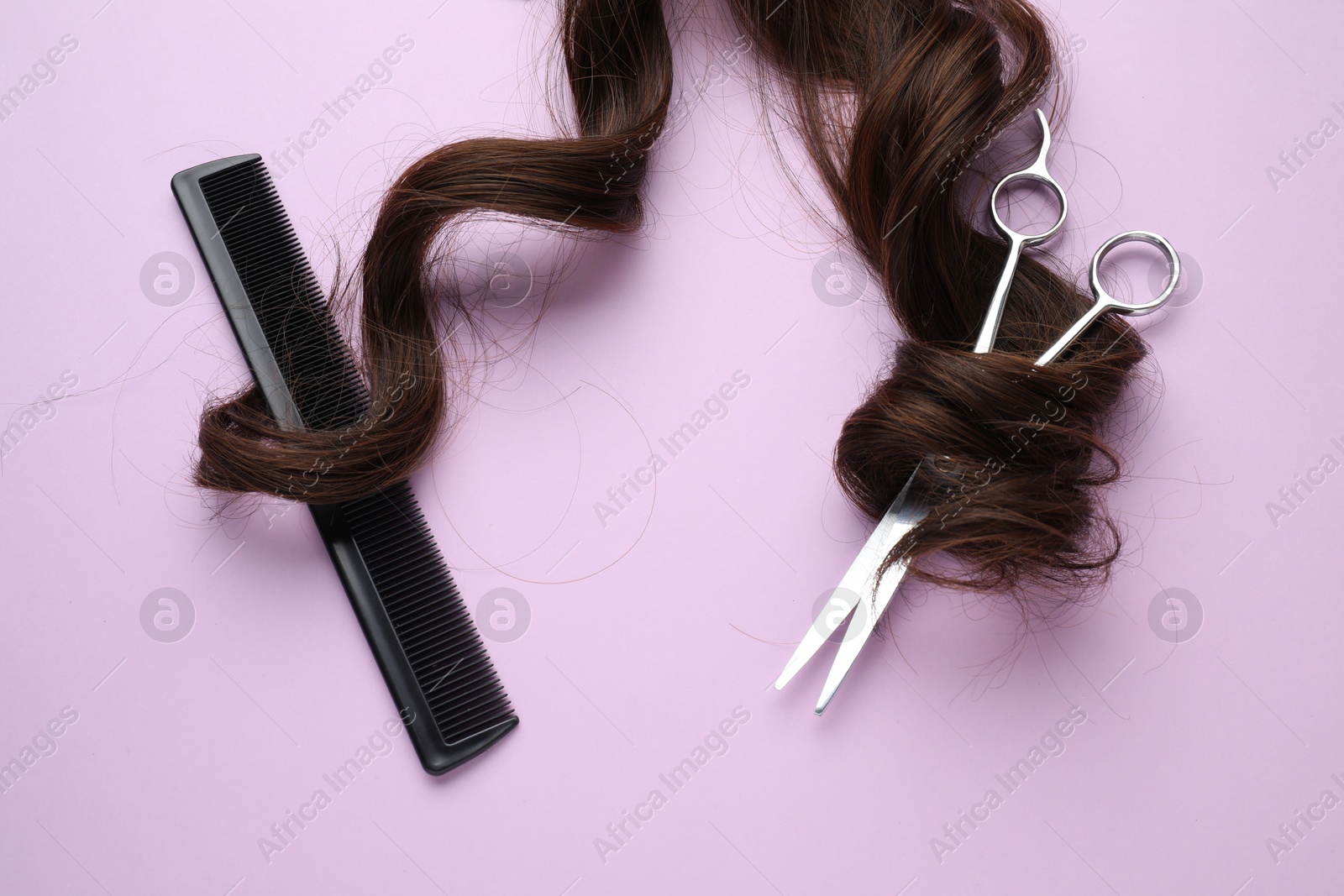 Photo of Brown hair strand, comb and professional scissors on violet background, top view