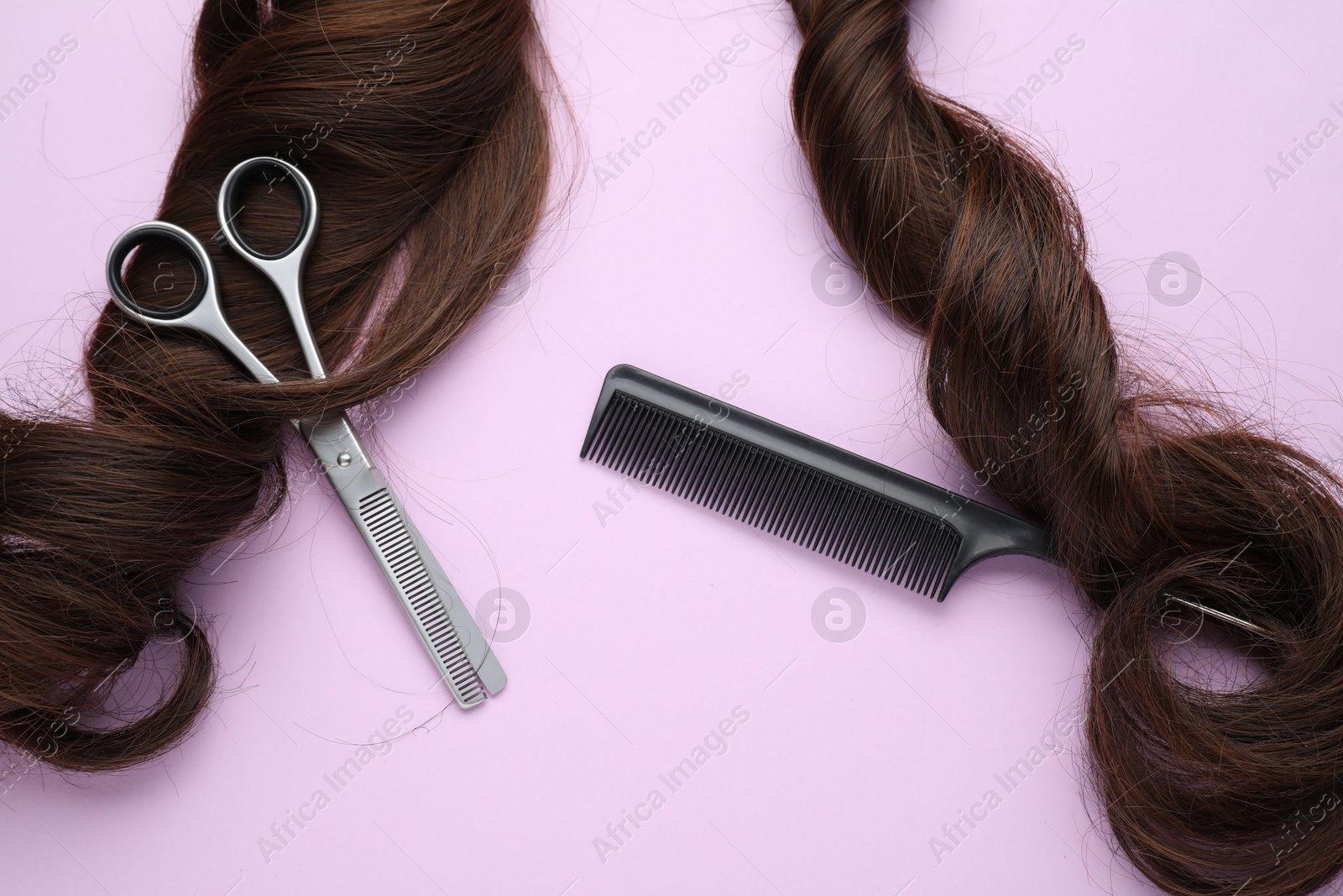 Photo of Brown hair strand, comb and professional scissors on violet background, top view