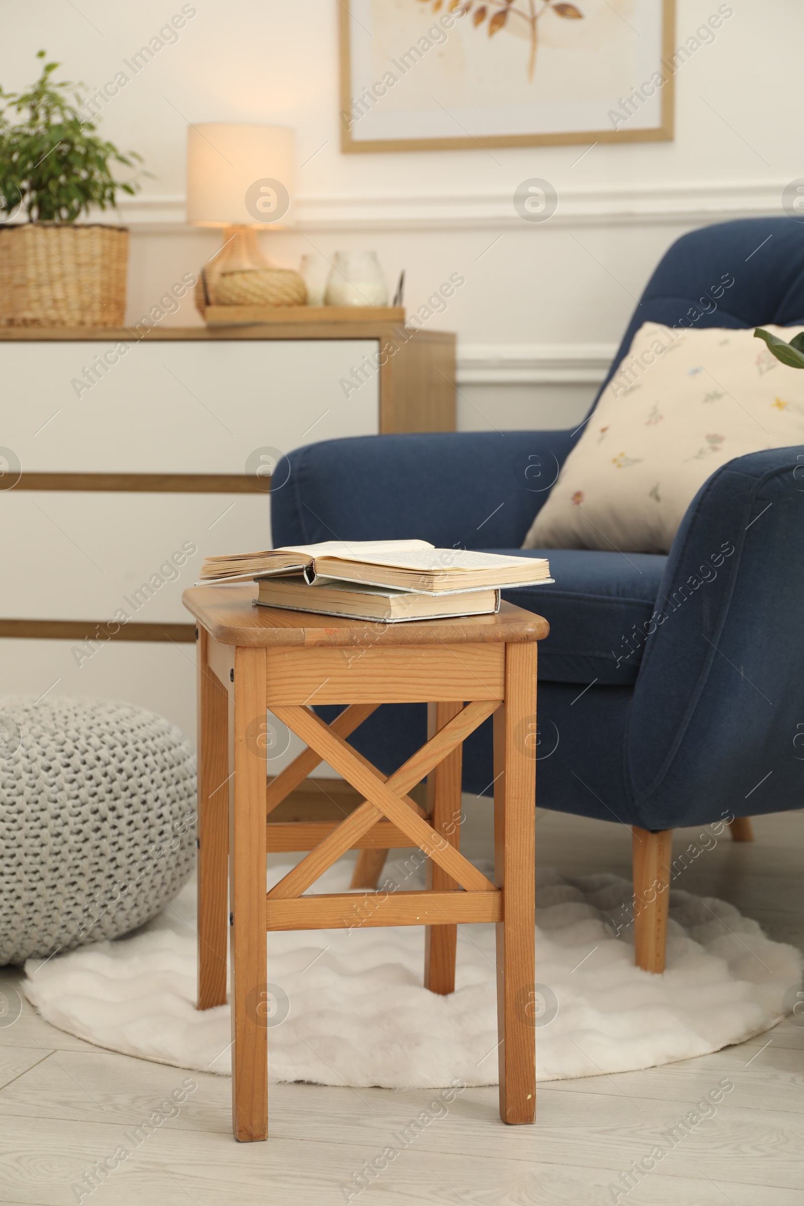 Photo of Stool, books, armchair and houseplant in room. Interior design