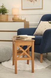 Stool, books, armchair and houseplant in room. Interior design