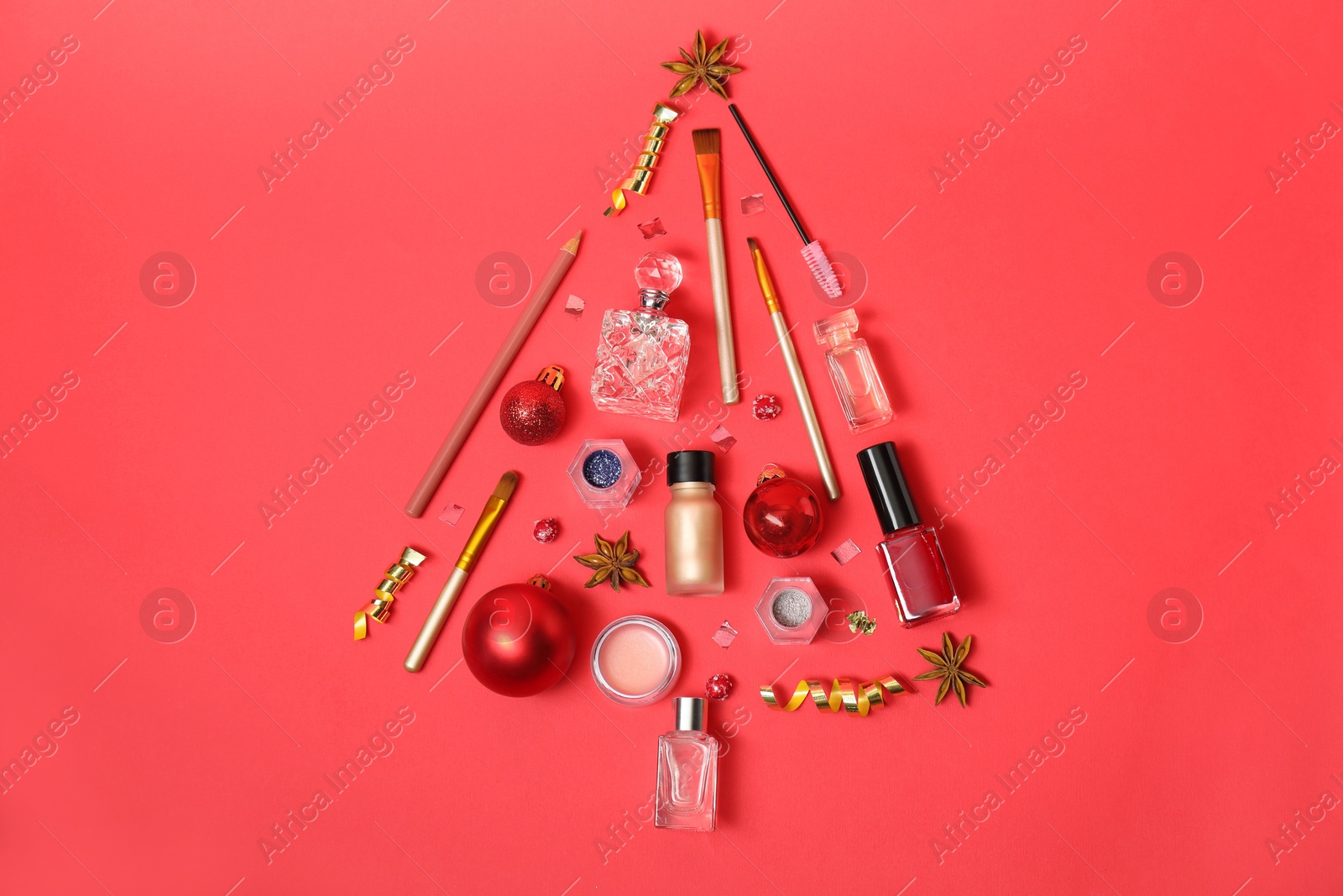 Photo of Christmas tree made of perfume bottles and makeup products on red background, flat lay