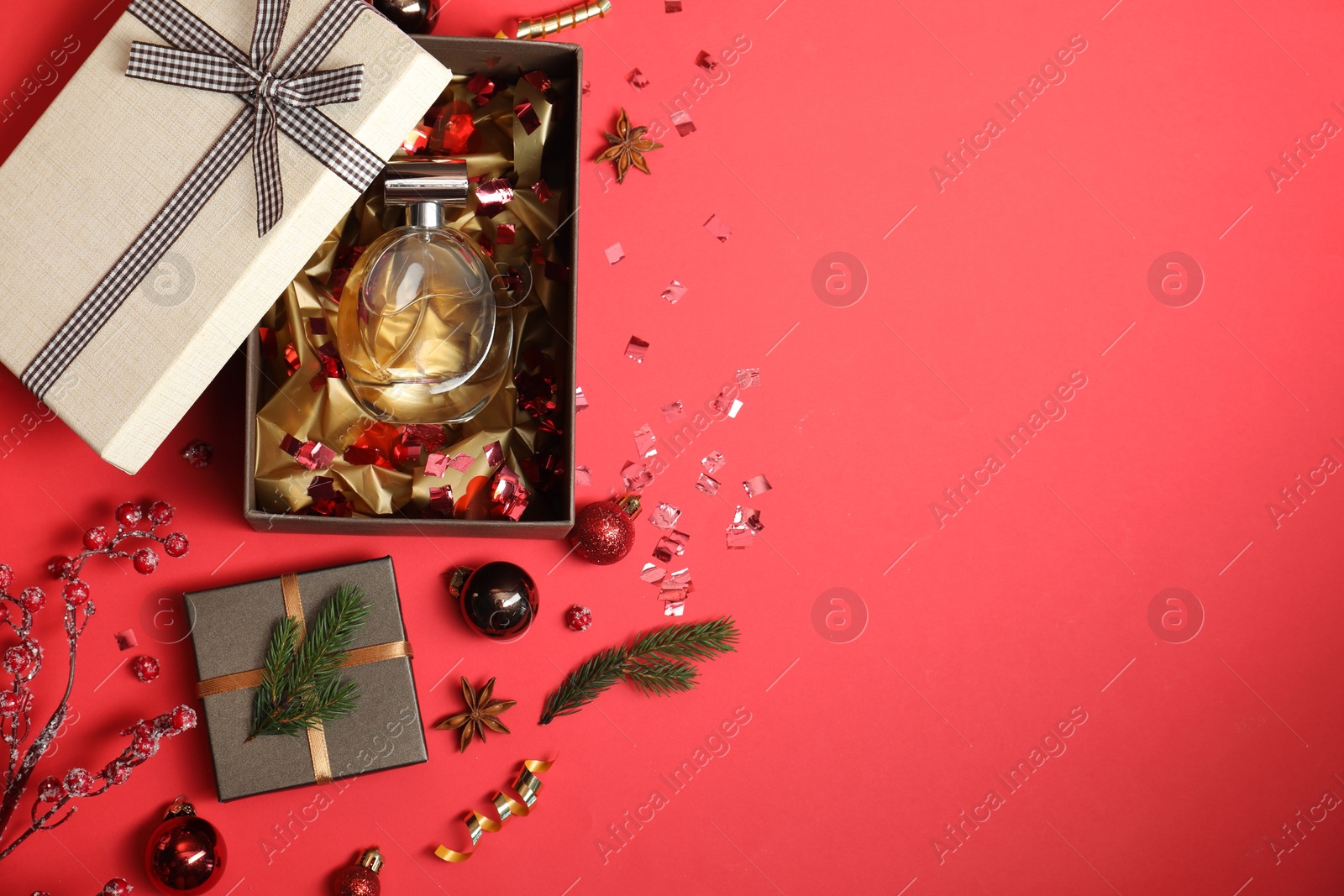 Photo of Perfume bottle in gift box and Christmas decor on red background, flat lay. Space for text