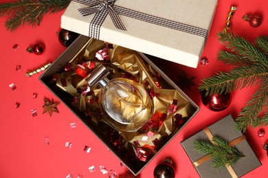 Perfume bottle in gift box and Christmas decor on red background, flat lay