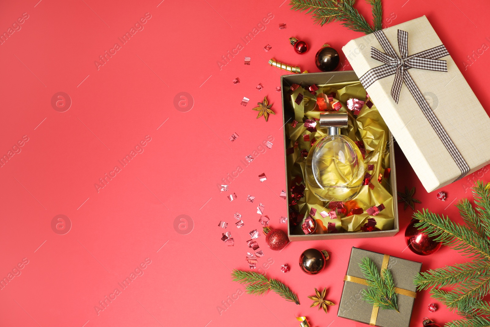 Photo of Perfume bottle in gift box and Christmas decor on red background, flat lay. Space for text