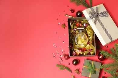 Photo of Perfume bottle in gift box and Christmas decor on red background, flat lay. Space for text