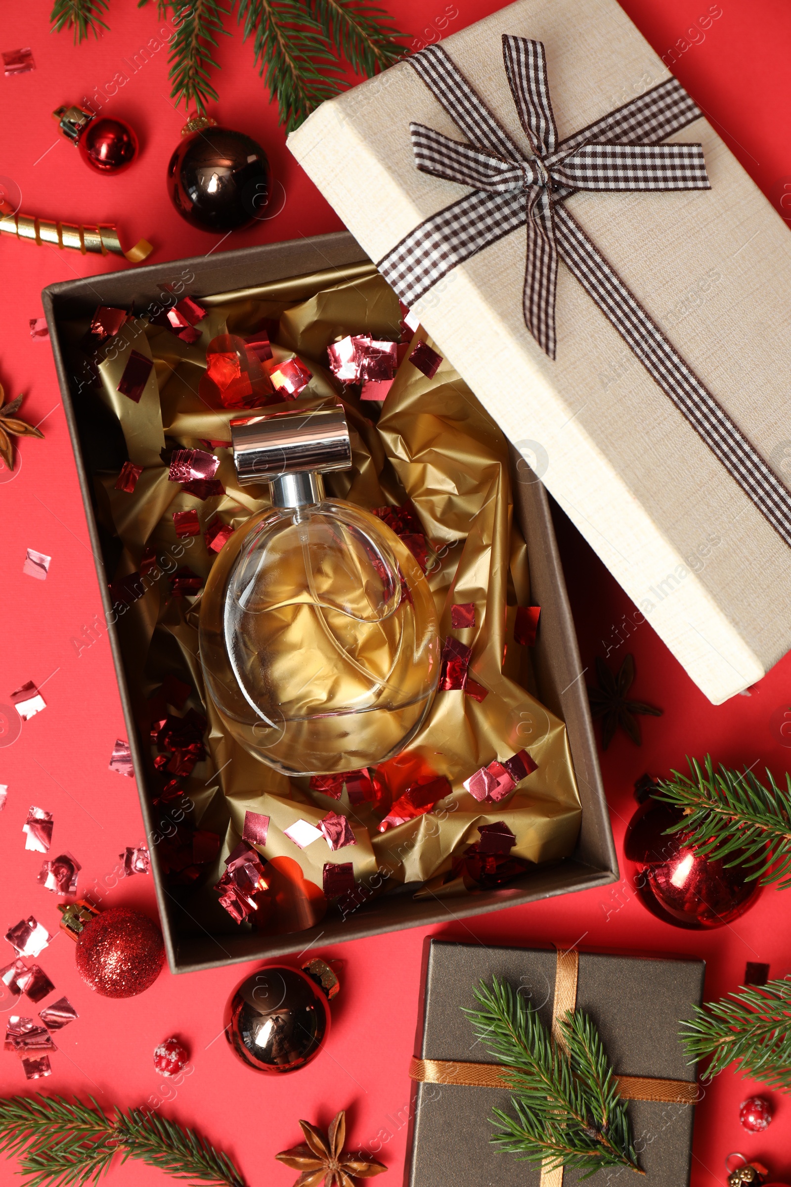 Photo of Perfume bottle in gift box and Christmas decor on red background, flat lay