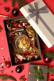 Photo of Perfume bottle in gift box and Christmas decor on red background, flat lay