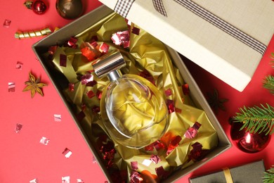 Perfume bottle in gift box and Christmas decor on red background, flat lay