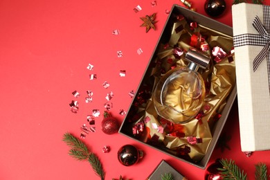 Photo of Perfume bottle in gift box and Christmas decor on red background, flat lay. Space for text