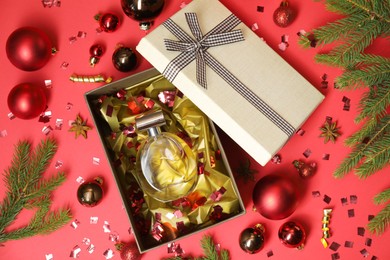 Photo of Perfume bottle in gift box and Christmas decor on red background, flat lay