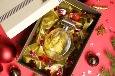 Perfume bottle in gift box and Christmas decor on red background, flat lay